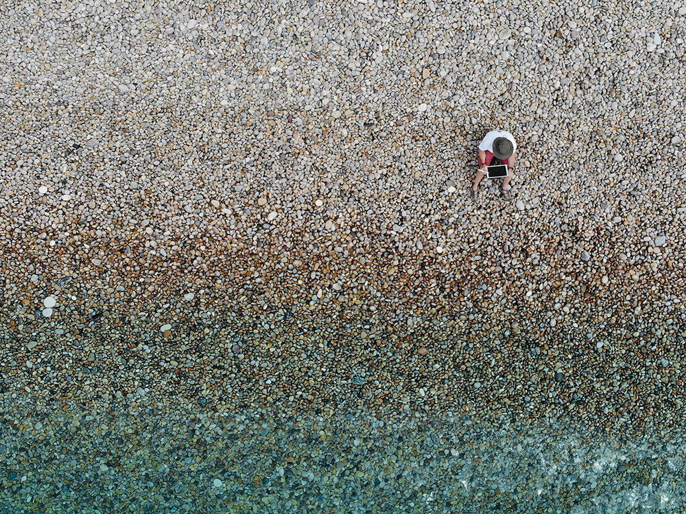 Foto de drone de um cara usando um tablet de maçã na praia