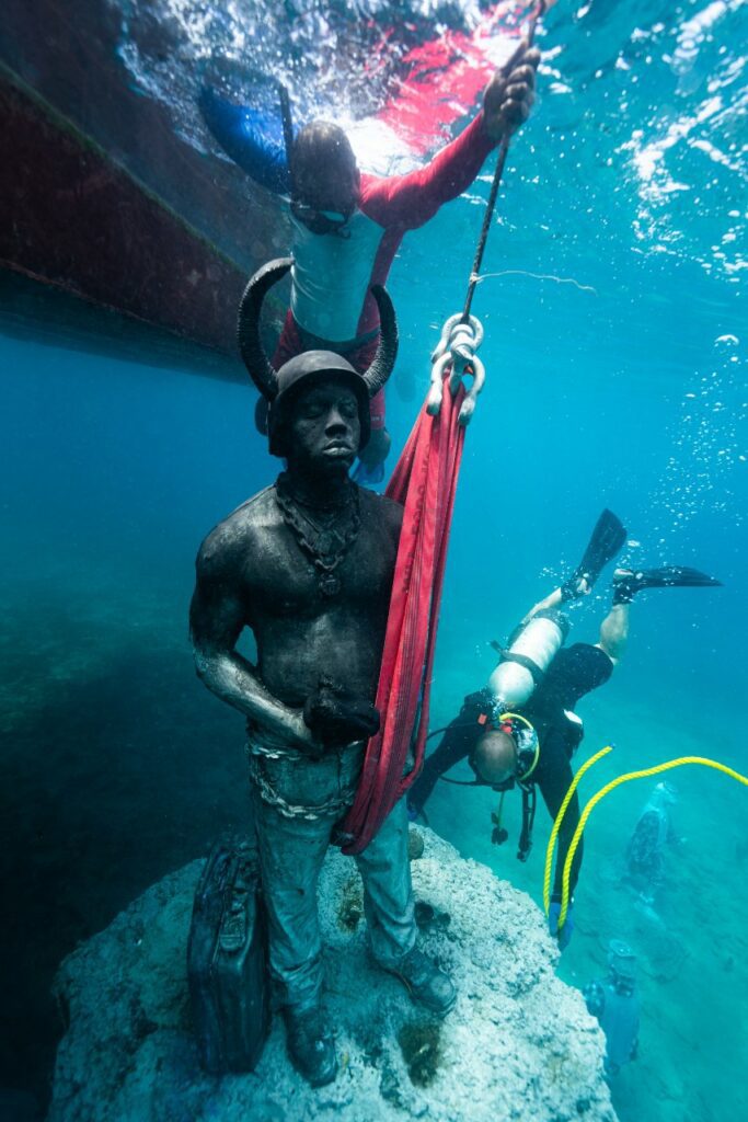 Divers work to install a Jab Jab sculpture in the Molinere sculpture park in Grenada
