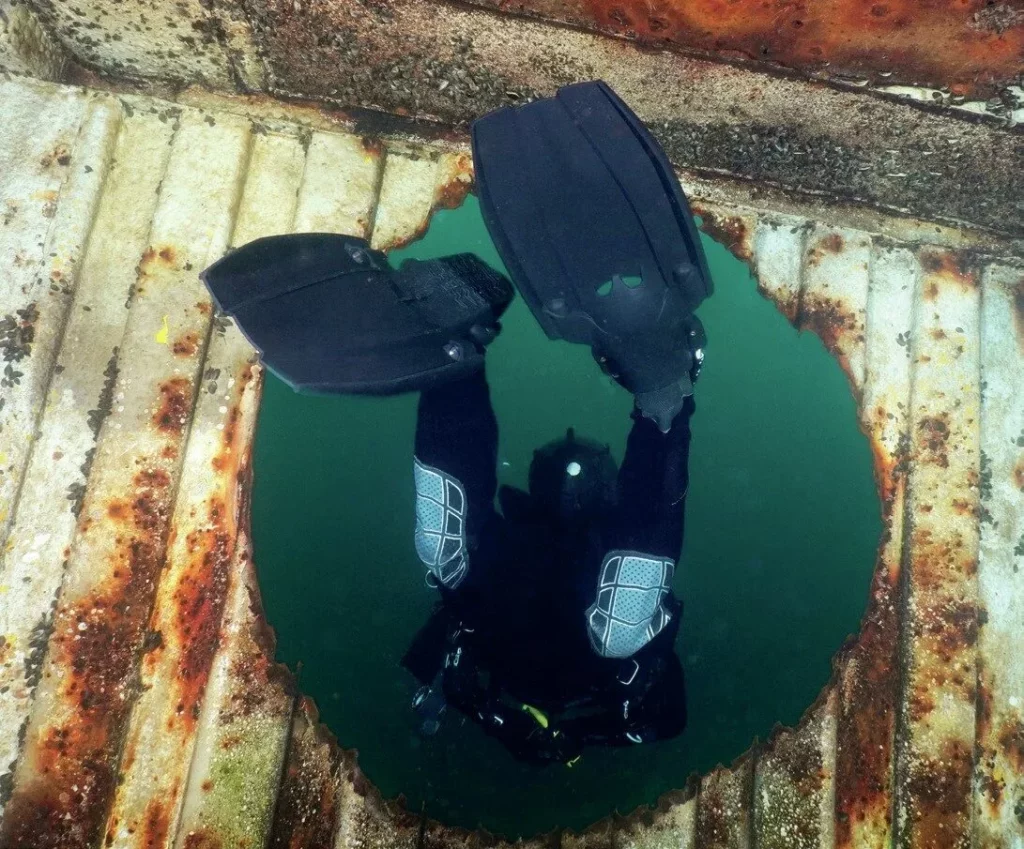 A diver flutter kicks through a hole in a wreck wearing Halcyon Vector Pro fins without kicking up silt