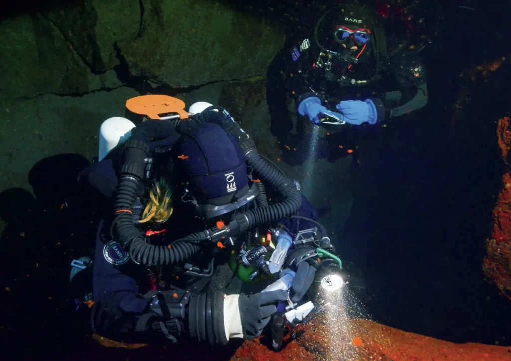 Iceland’s Underwater Frontier: Science in Silfra 7 A technical diver carefully collecting delicate microbial biofilm samples from a rock face in Silfra Hellir.