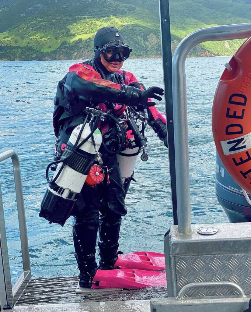 A scuba diver in a drysuit geared up and ready to descend into the waters of Port Gore to explore the Mikhail Lermontov cruise liner wreck.