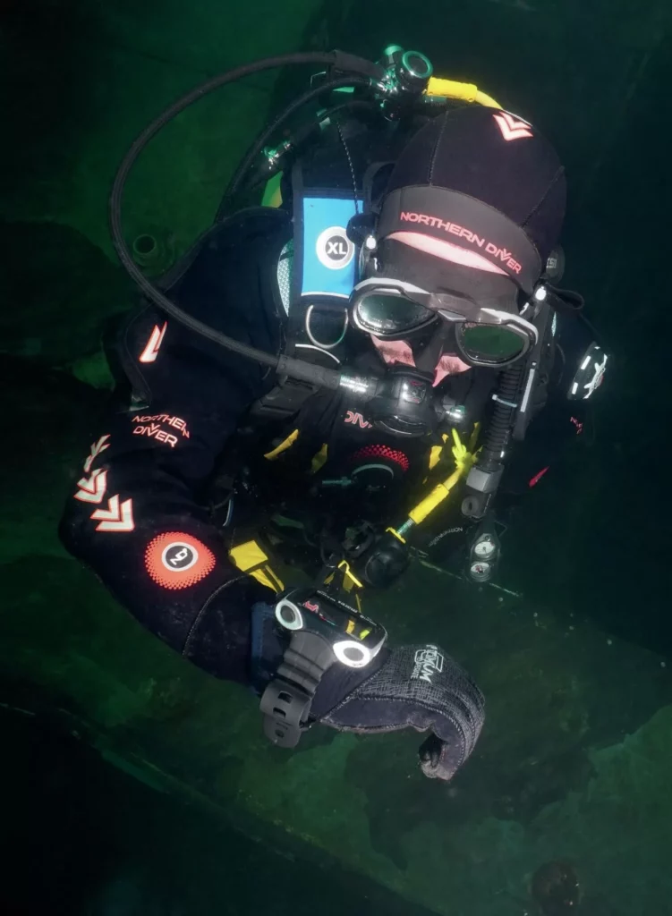 A scuba diver in green, temperate water checking his dive computer to monitor depth and nitrogen limits.