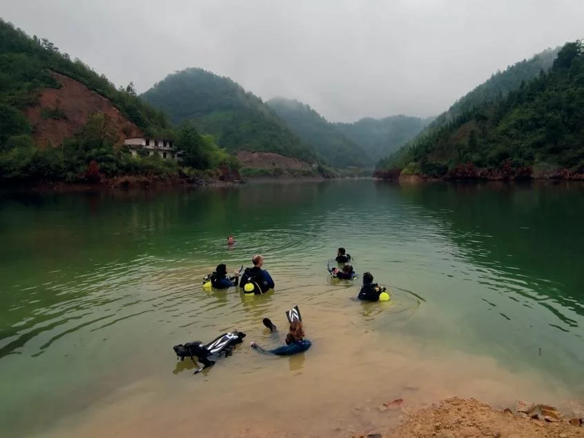 Group of scuba divers in drysuits at the water's surface preparing for a descent into Qian Dao Lake.