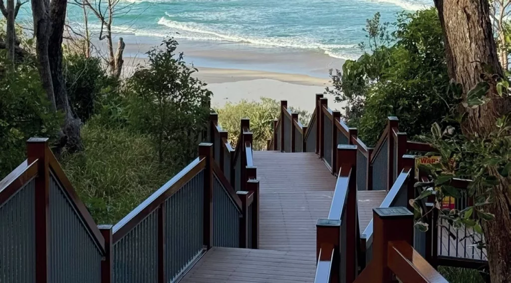 wooden stairway leading up a hill on a coastal trail, offering panoramic views of beautiful beaches and the ocean.