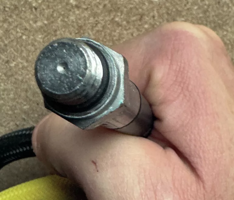 Close up of a 7/16 inch high-pressure scuba hose showing the small flow restriction hole for safety.