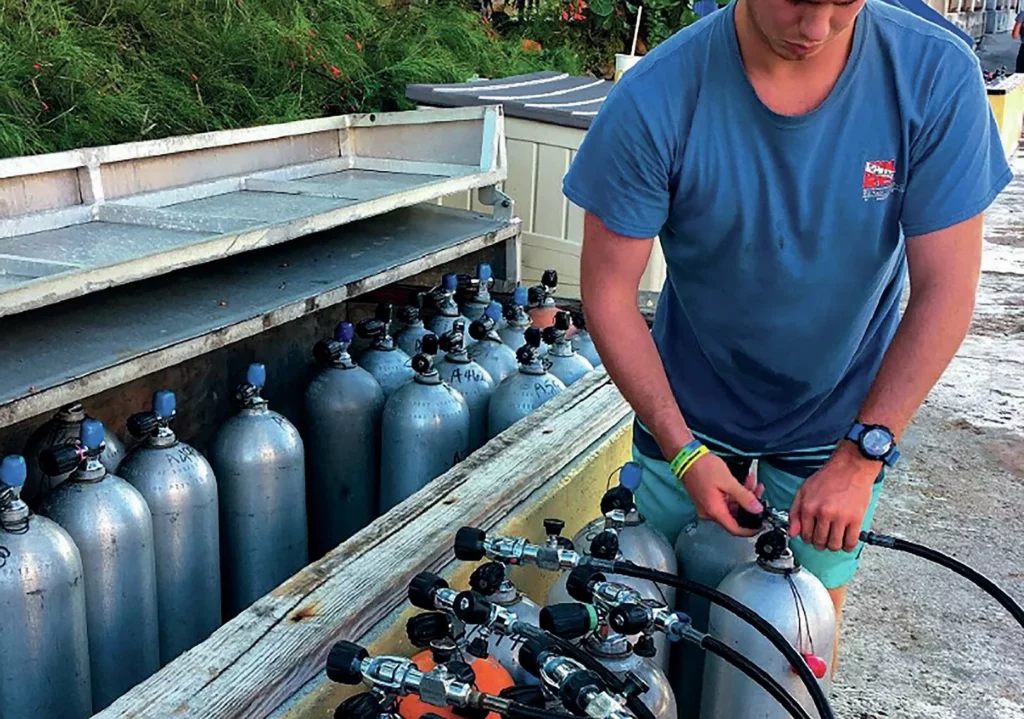 A dive technician monitoring a high-pressure compressor and filtration system to maintain scuba air purity and prevent gas contamination.