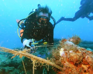 A diver in murky water cutting away discarded fishing line that could easily trap a turtle