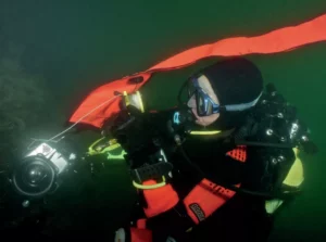 A scuba diver underwater carefully deploying a delayed surface marker buoy as part of their essential safety gear.