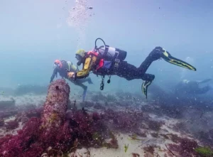 Two divers examining a Colossus cannon standing proud on the seabed (CISMAS)