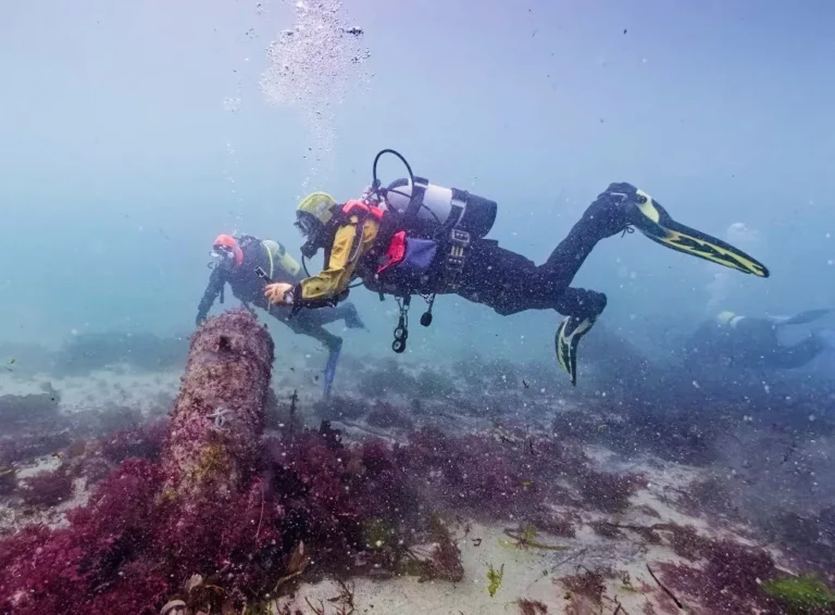 Two divers examining a Colossus cannon standing proud on the seabed (CISMAS)