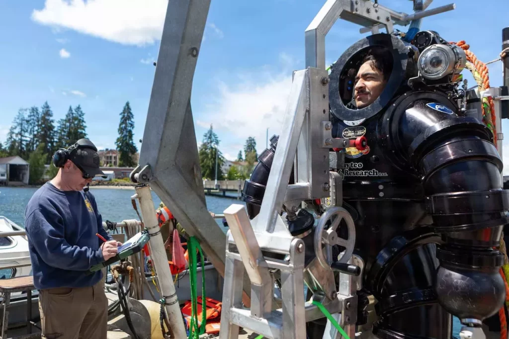 DSEND no-deco divers evolve from pool to seabed 3 Navy divers monitor the internal systems of a DSEND suit as others lower the suit into the water during a training exercise in Liberty Bay (US Navy)