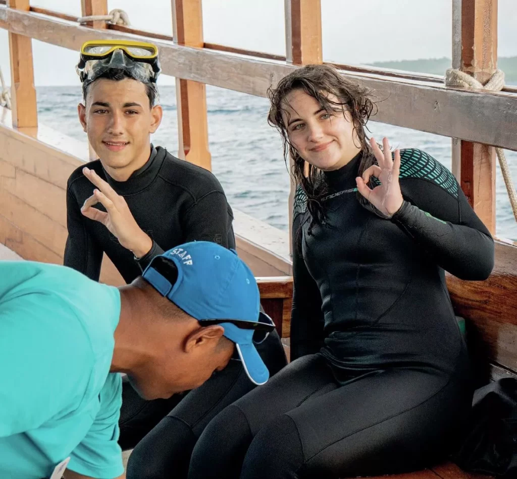 Sibling dive buddies Aura and Ian smiling together on the deck of a spacious dive boat after an ocean excursion.